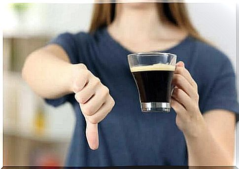 A woman holds a cup of coffee in her hand and puts her thumbs down